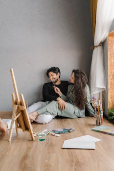 A couple smiles while painting together at home, capturing relaxation and creativity.