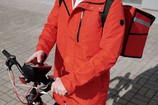 A delivery cyclist using a smartphone, wearing a vibrant red jacket outdoors.