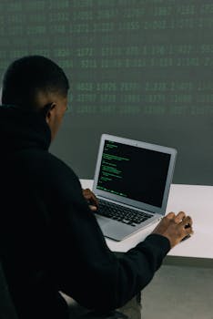 A programmer engaged in coding on a laptop in a tech-focused workspace with a digital interface.