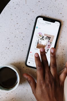 Close-up of hand scrolling Instagram on smartphone near coffee cup on table.